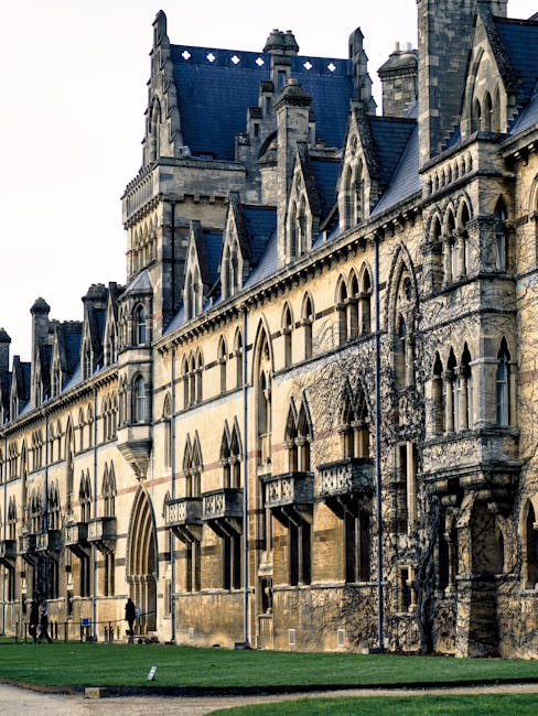 The image shows the upper section of a historic building with a tall, pointed tower topped by a copper-green spire and a decorative clock face. The tower's stonework features detailed gothic-style arc